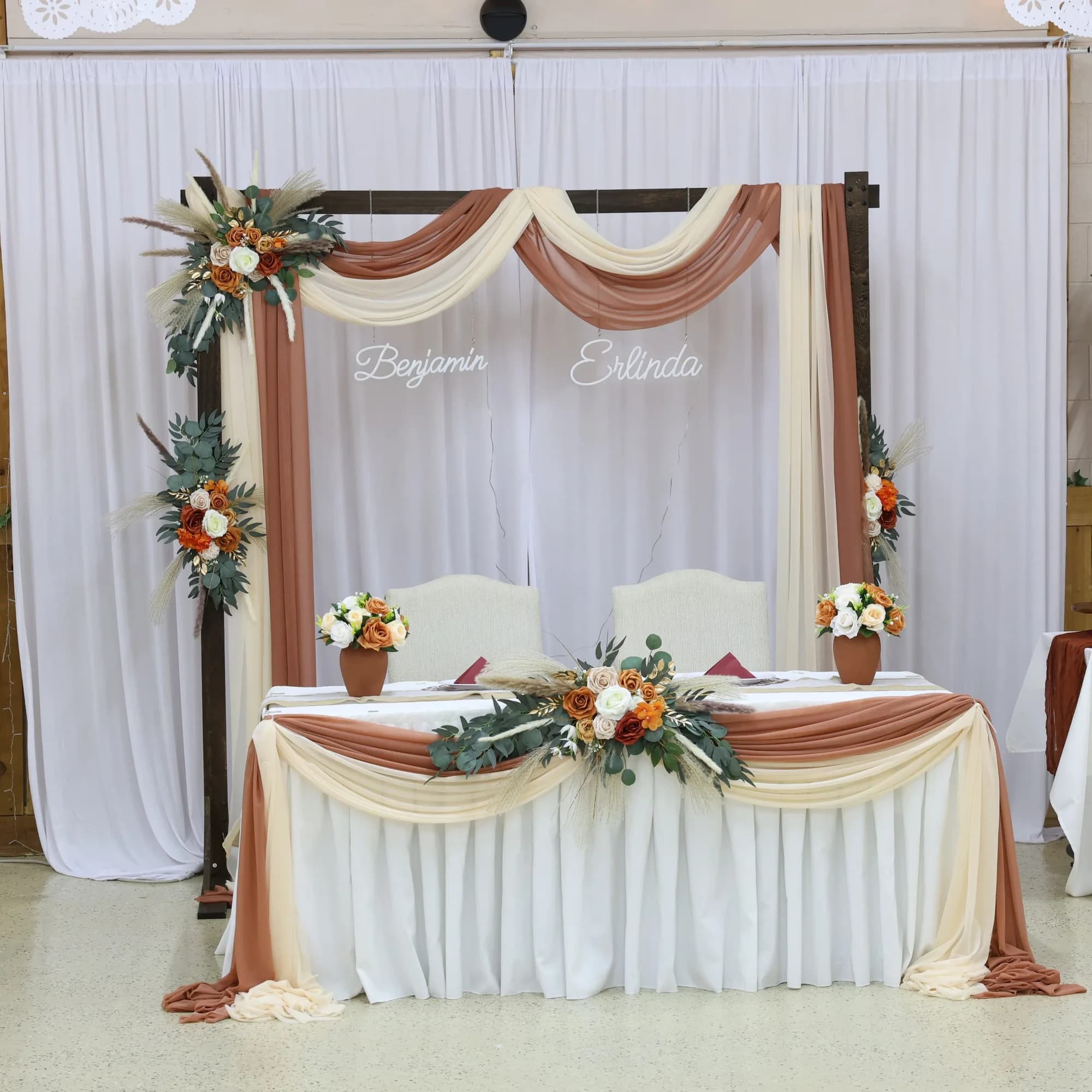Wedding sweetheart table arch dressed in rust and cream drapery